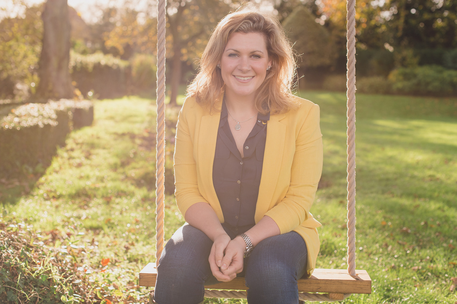 Wedding planner Natasha Spencer headshot sitting on a wooden swing in a formal garden setting