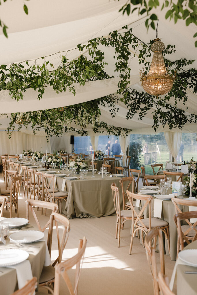 Inside a clear span marquee with smilax ceiling decor, empire chandeliers and draping, soft green table linen and ivory candles