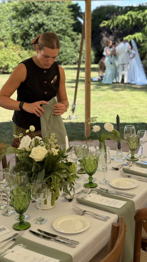luxury marquee wedding planner adjusting final table settings as bridal party enjoy their drinks reception in the background