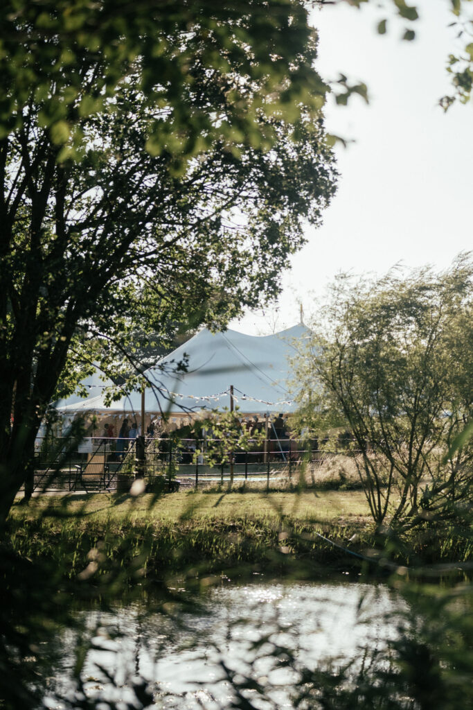 sailcloth marquee shown through trees over pond at country estate