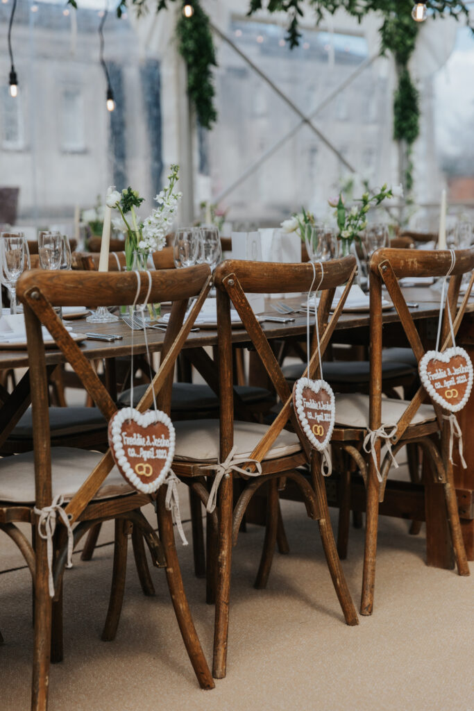 traditional German wedding cookies hanging off the back of cross back chairs in a clear roof marquee