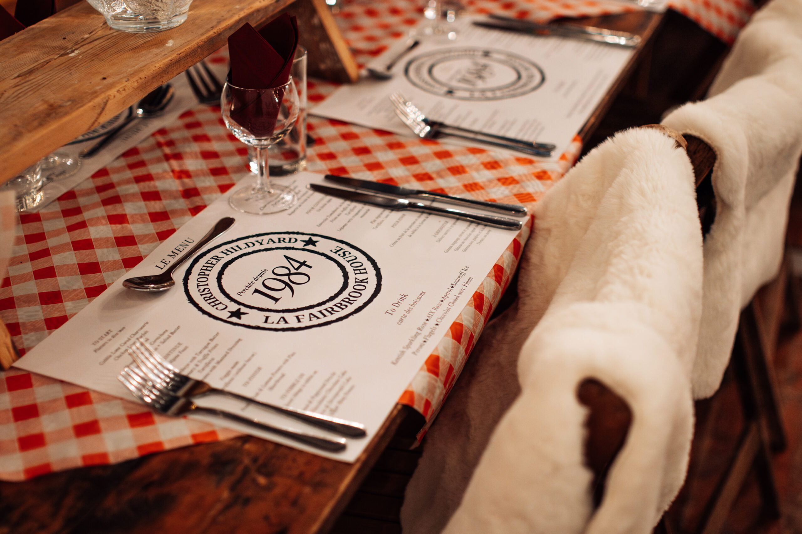 Close up of a table for a winter party with a personalised and branded place mat and red and which checked table cloth.